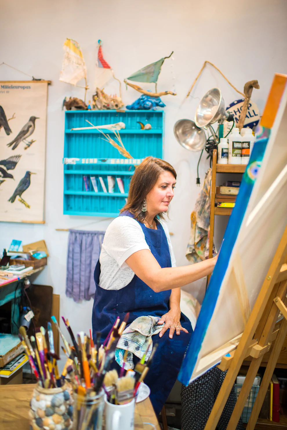 Leslie Campbell of Ravenworks Studio sitting at an easel and painting in her studio women we know over 40 SSM Creative Collective